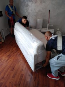 sťahovanie bytov a domov. preprava sedačky. dvaja pracovníci nosia sedačku